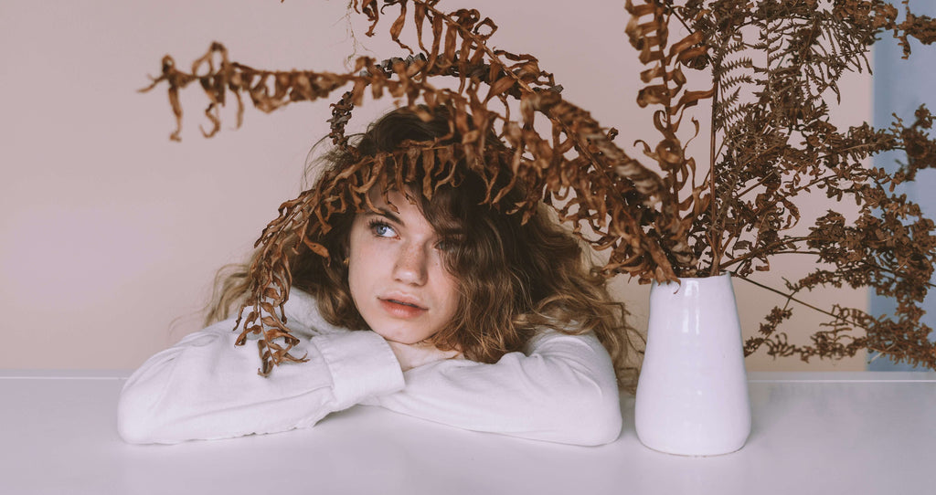 woman with brown wavy hair resting head under plant